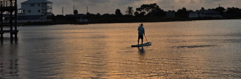 Person paddleboarding at sunset on calm water, representing memorable travel experiences.