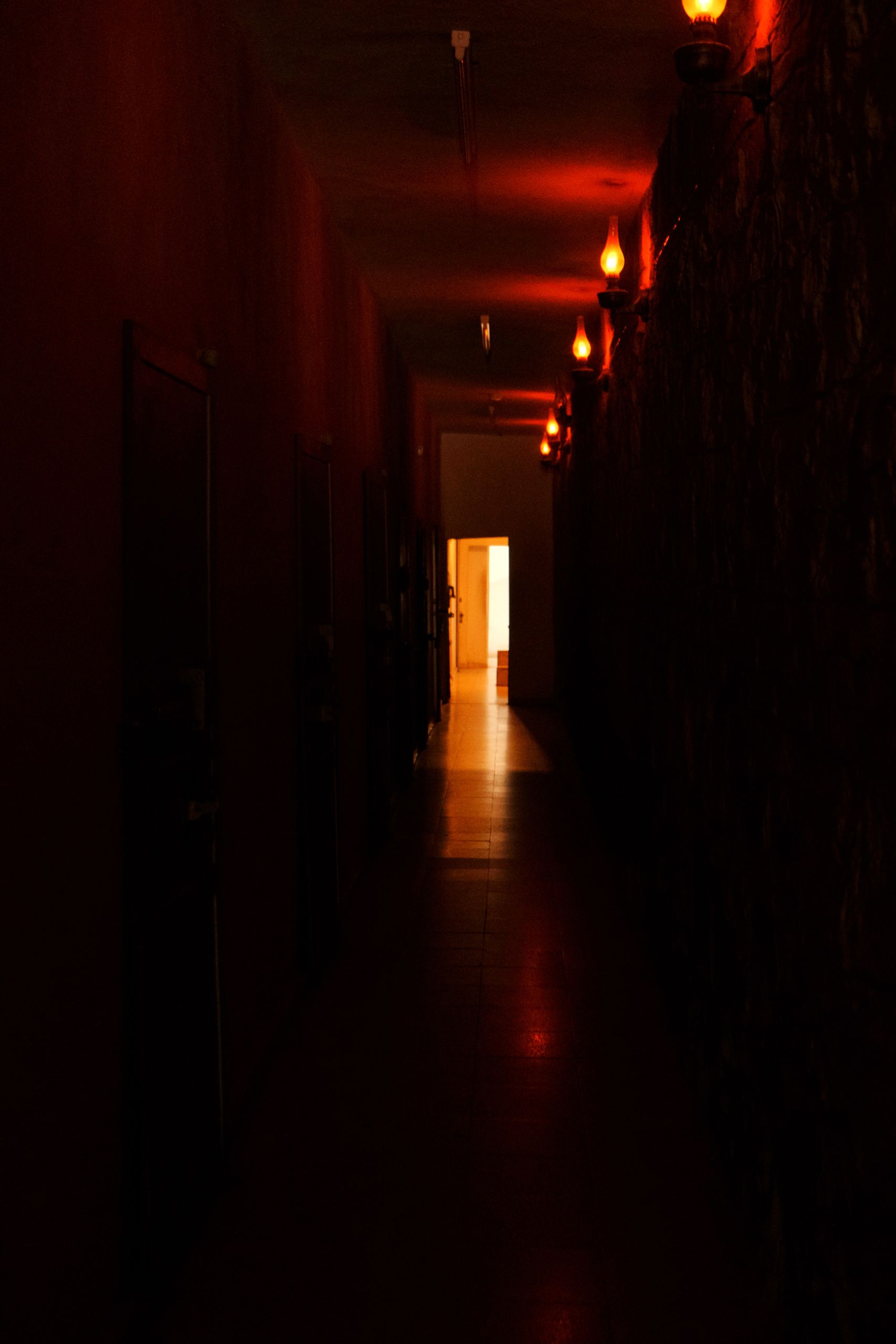 A dimly lit corridor with warm, dramatic lighting and a bright opening at the end.