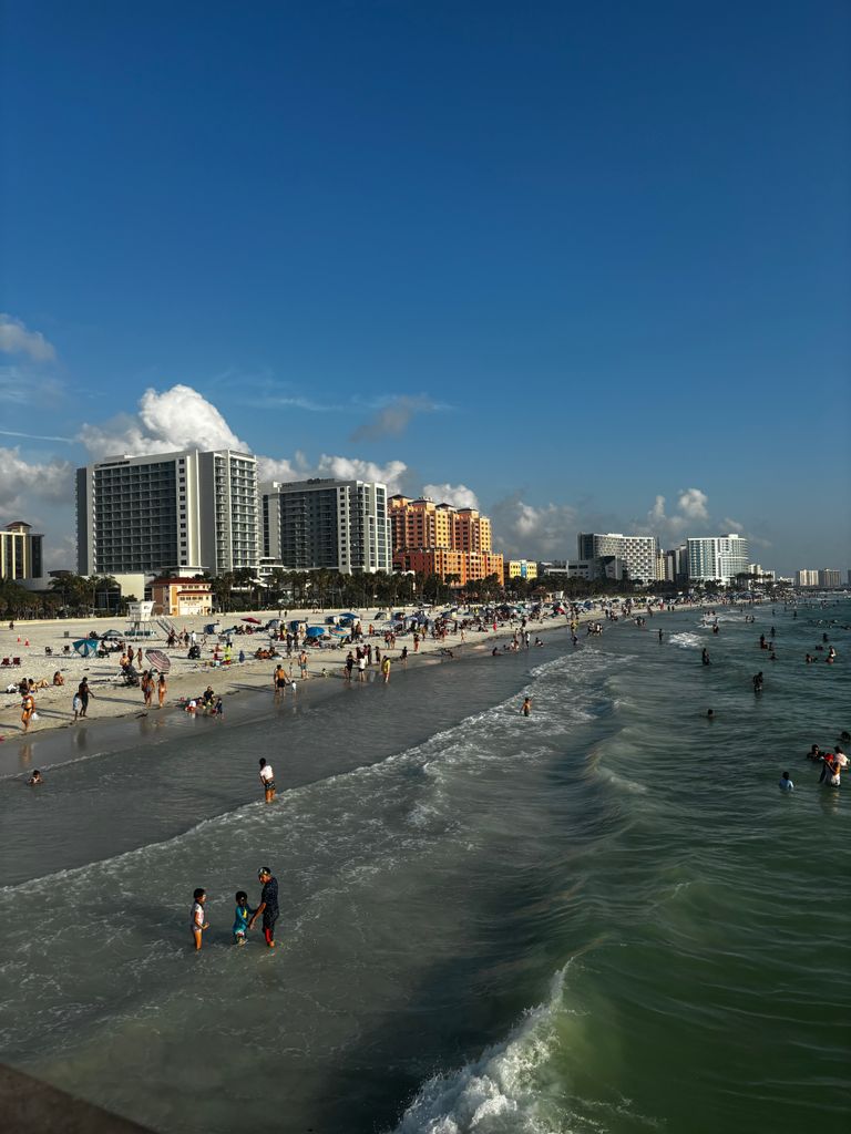 Beachgoers enjoy the sun and waves at Clearwater Beach with a scenic city backdrop.