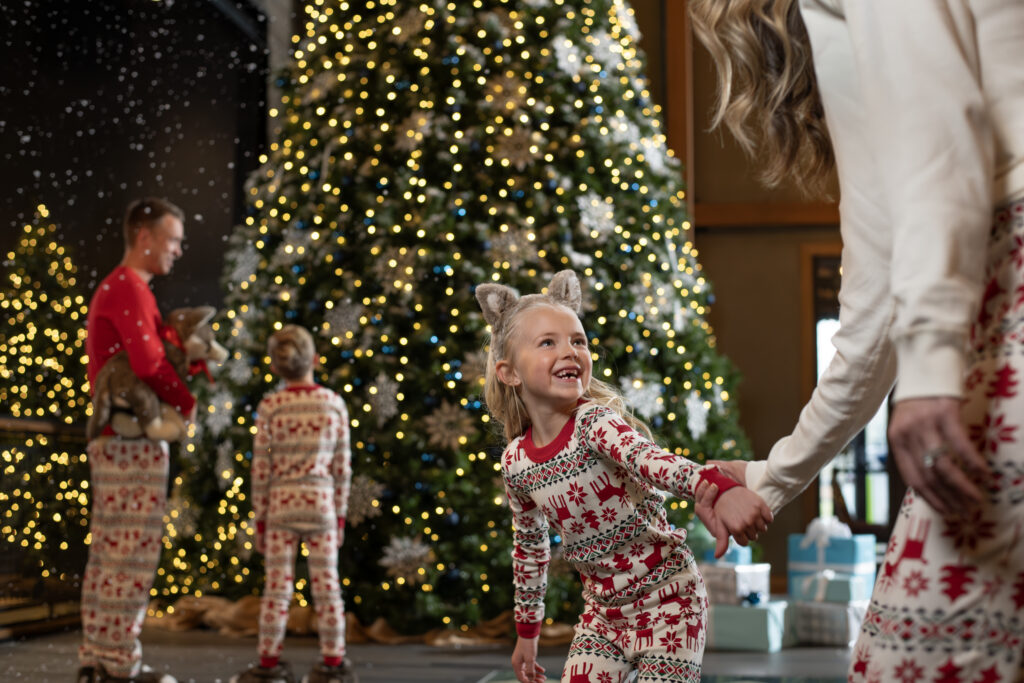 Child in Christmas pajamas beside a decorated Christmas tree during Snowland at Great Wolf Lodge